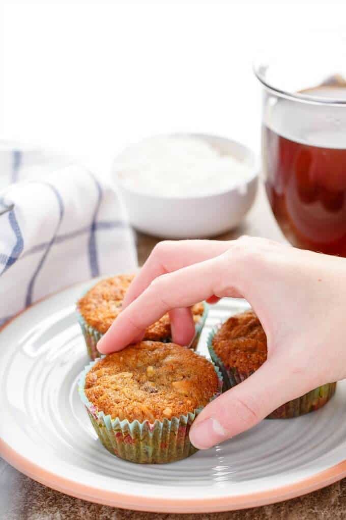 Chocolate Chip Banana Bread Muffins with Coconut & Nuts on plate touched by hand. Jar of liquor , bowl of coconut and cloth wipe in the background