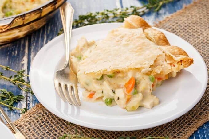 Homemade Turkey Pot Pie  on white plate with fork, herbs and glass tray on purple table