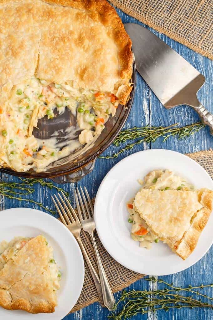 Homemade Turkey Pot Pie  on white plates and glass tray. Spatula, forks, herbs on blue table