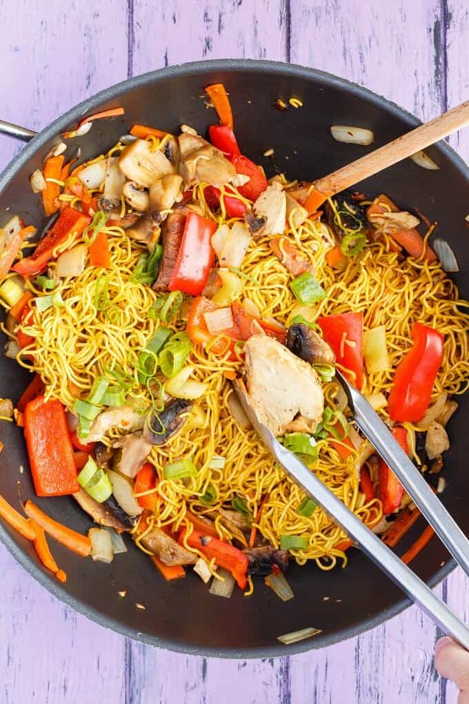 Leftover Turkey Stir Fry in black pan with kitchen tongs and wooden spatula on purple table