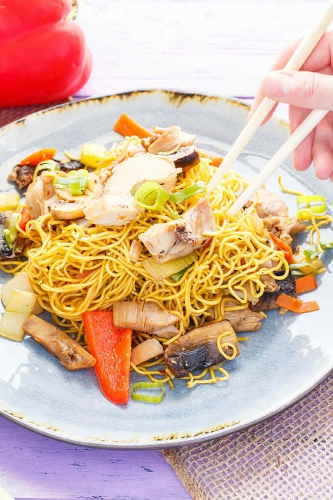 Leftover Turkey Stir Fry on blue plate with sticks held by hand, vegetable in the background