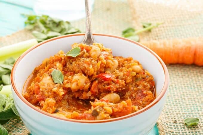 "Meaty" Vegetarian Chili  in orange white bowl with spoon, vegetable and herbs on blue table