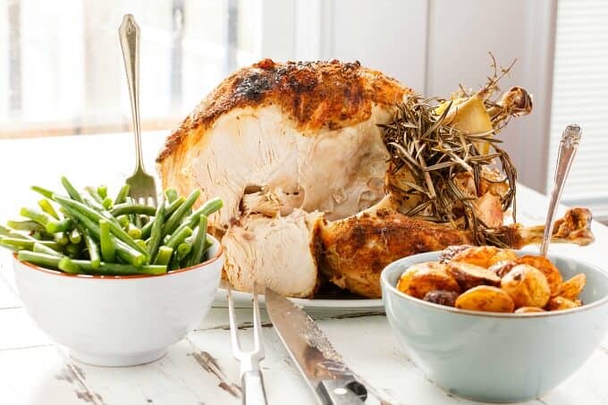 Slow Cooker Whole Turkey with herbs on white tray, bowls of asparagus with fork, bowls of potatoes with spoon , Knife and fork on white table