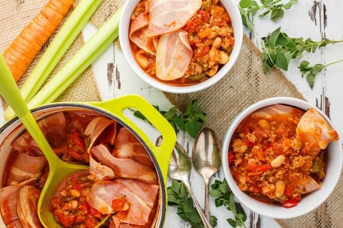 Turkey Bacon Chili in bowls and green pot with spatula. Vegetable, herbs and spoons on the table