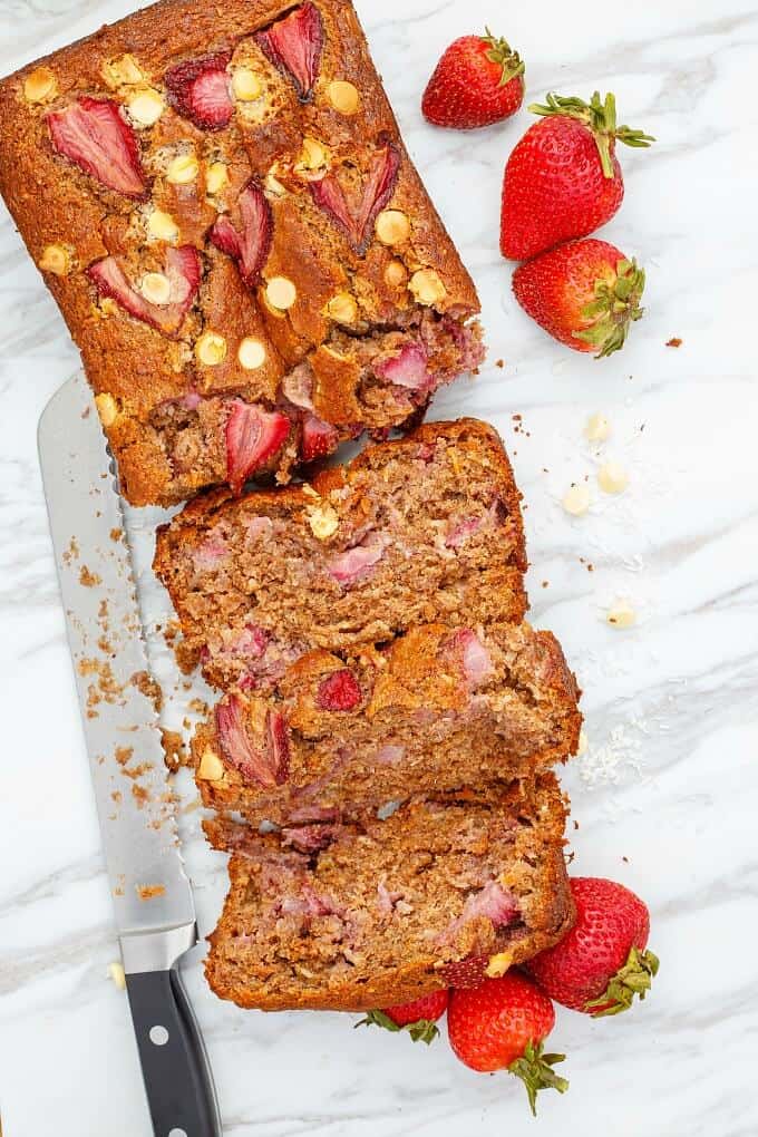 White Chocolate Strawberry Banana Bread partialy sliced with knife, ripe strawberries on gray table