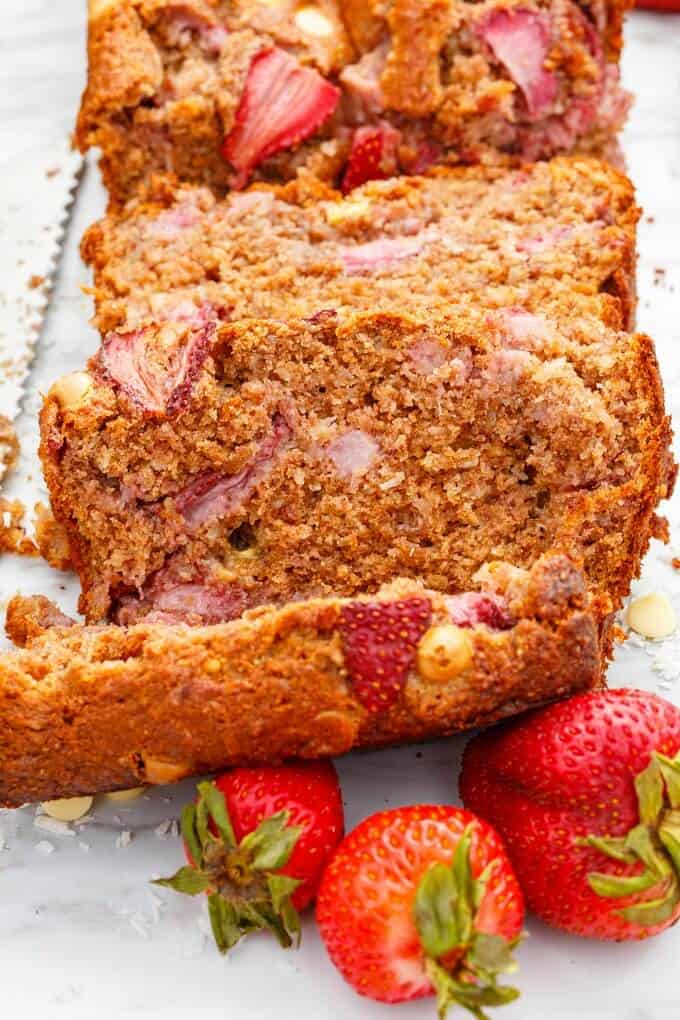 White Chocolate Strawberry Banana Bread partialy sliced with ripe strawberries on white background