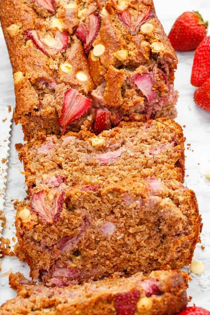 White Chocolate Strawberry Banana Bread partialy  sliced on white background with ripe strawberries