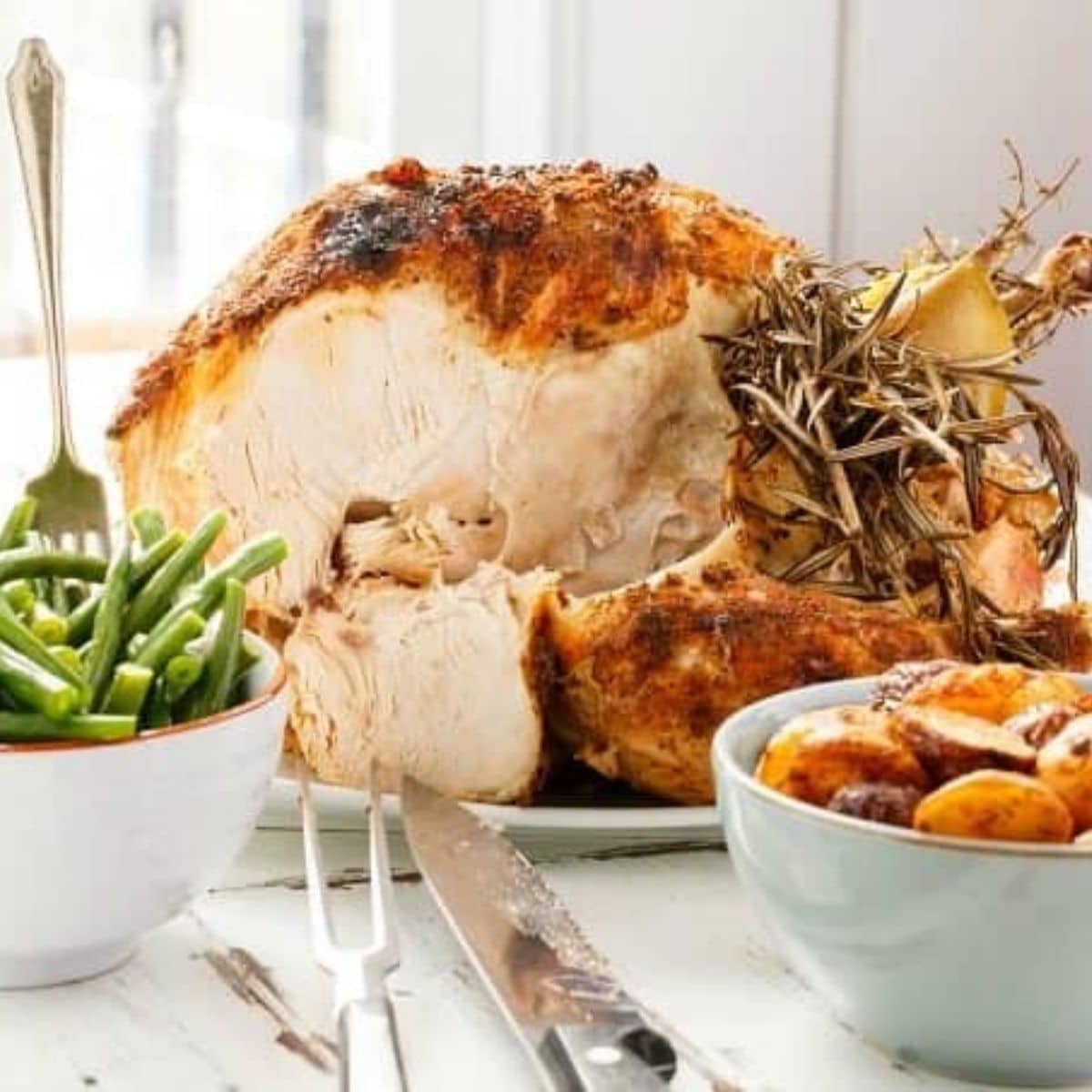 Slow cooker whole turkey on tray with bowls of asparagus and potatoes with knife and fork on table
