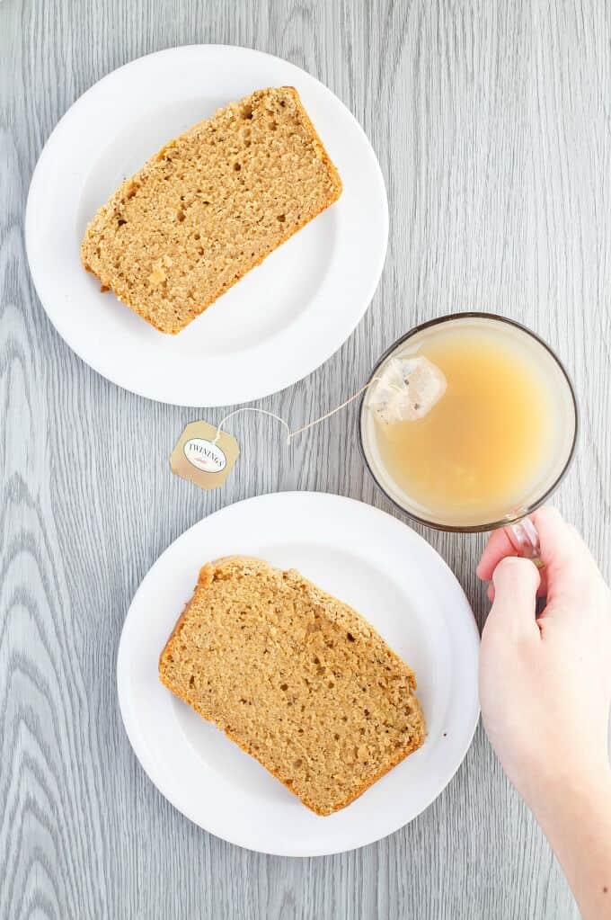 Earl Grey Tea Bread  slices on white plates, cup of tea held by hand on gray table