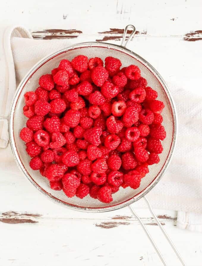 Raspberries on strainer over cloth wipe on white brown table