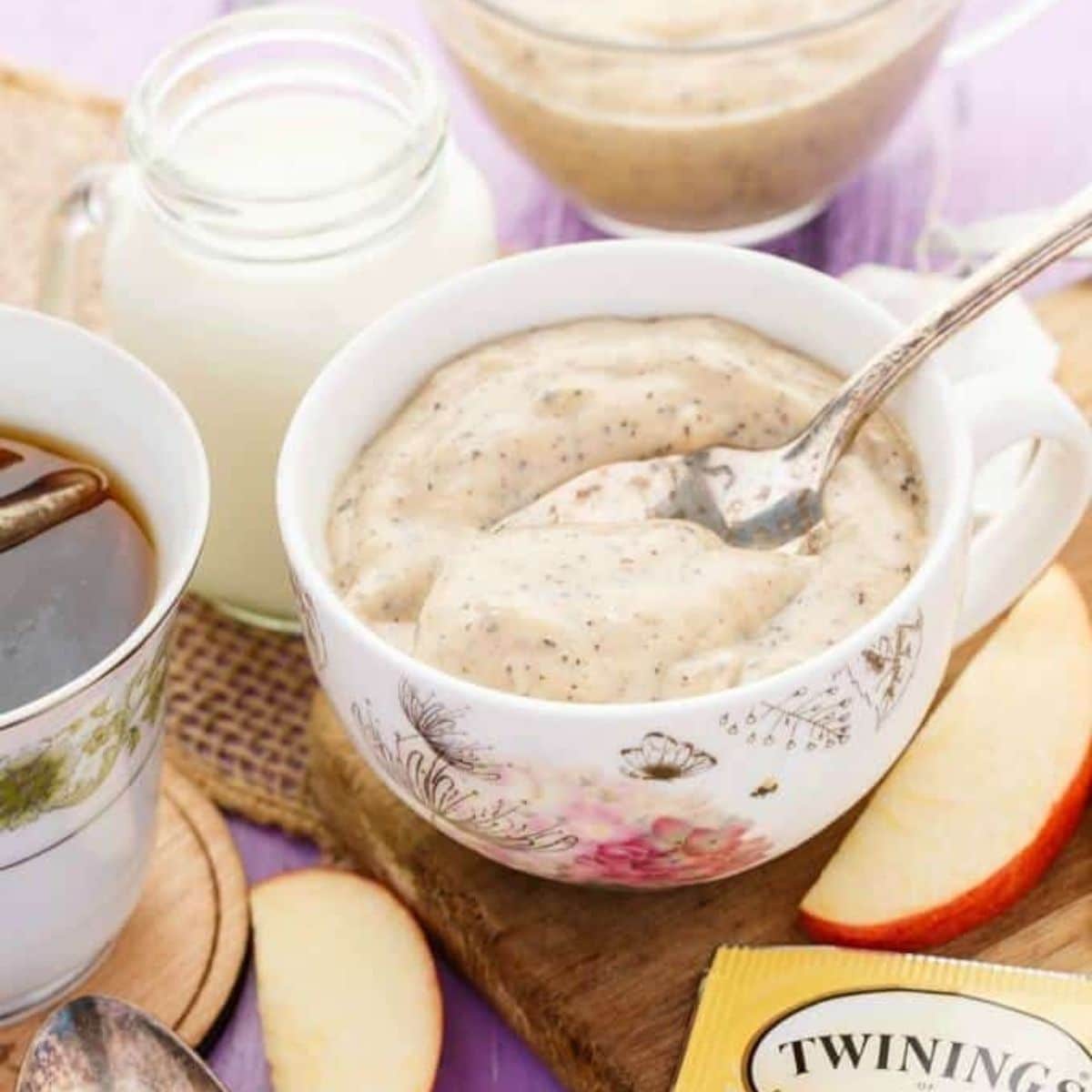 Earl grey pudding on bowl with spoon on wooden pad with slices of apple, cup of tea and jar of milk