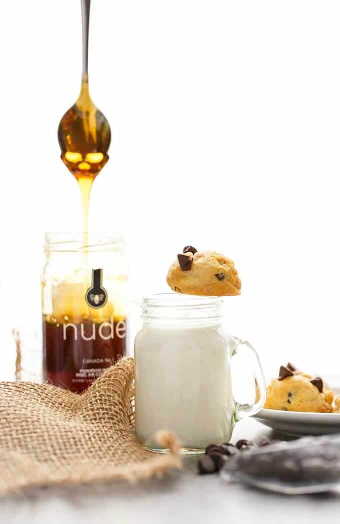 Honey Chocolate Chip Cookies on white plate, on jar of milk. Spoon over jar of honey, chocolate chips, brown cloth on table