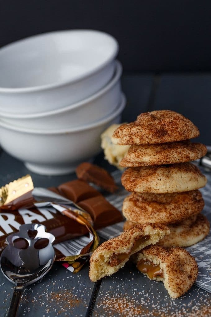 Caramilk Stuffed Snickerdoodles with spoon, cloth wipe, chocolate candy, white bowls on gray table