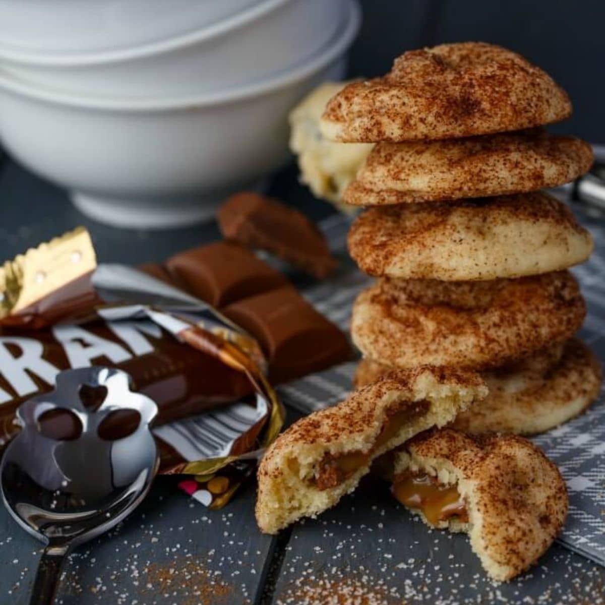 Caramilk stuffed snickerdoodles with spoon, candy and white bowls on brown table