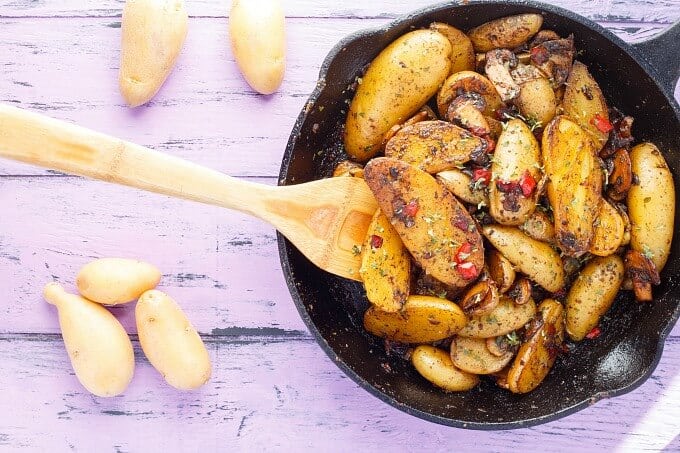 Breakfast Home Fries (using Fingerling Potatoes!) in black pan with wooden spatula on purple table with potatoes