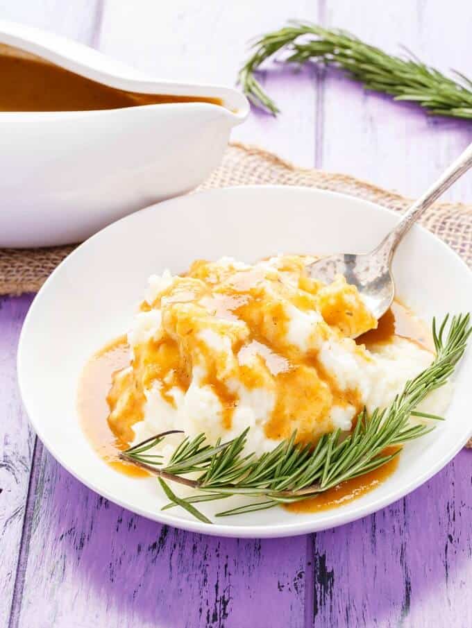 Homemade Turkey Gravy on white plate with mashed dish,herbs and spoon. Herbs, brown cloth, white bowl with sauce on purple table