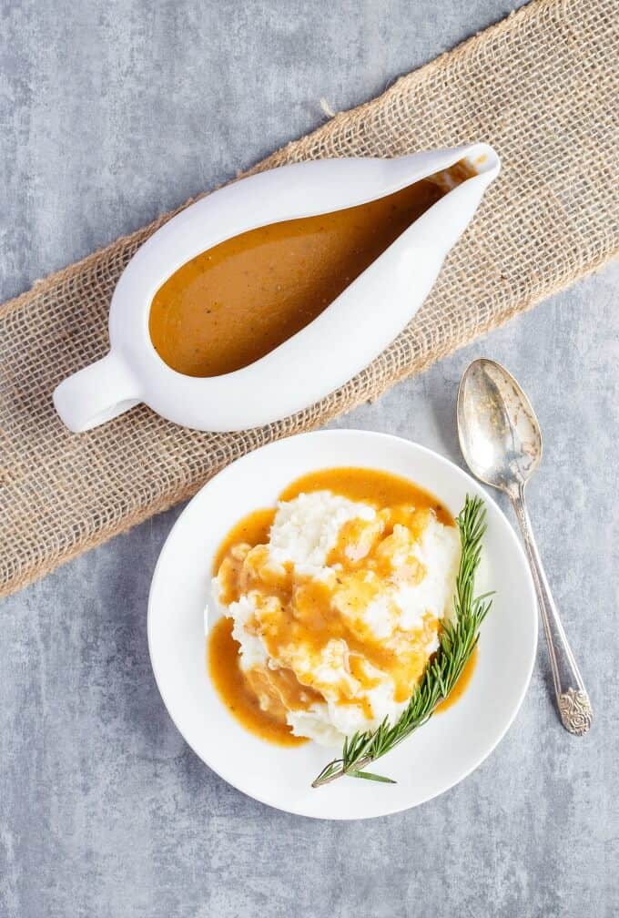 Homemade Turkey Gravy in white bowl and on white plate with dish and herb next to spoon on gray table