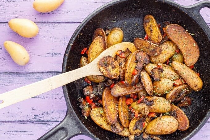 Vegetarian Home Fries (using Fingerling Potatoes!) on black pan with wooden spatula on purple table with potatoes