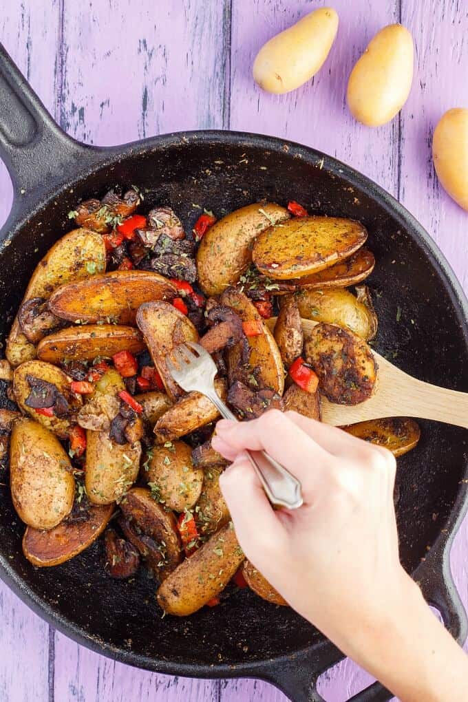Vegetarian Home Fries (using Fingerling Potatoes!) in black pan with wooden spatula, fork held by hand, on purple table with potatoes
