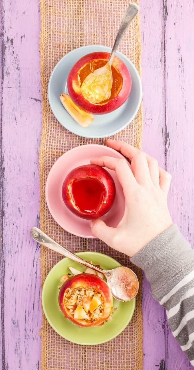 Edible Apple Cups  on small colorful plates on brown cloth on purple table. One cup held by hand.