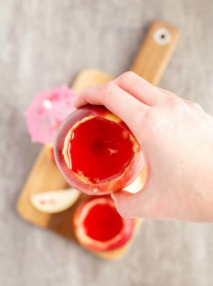 Edible Apple Cup held by hand over wooden pad with edible apple cups with umbrella