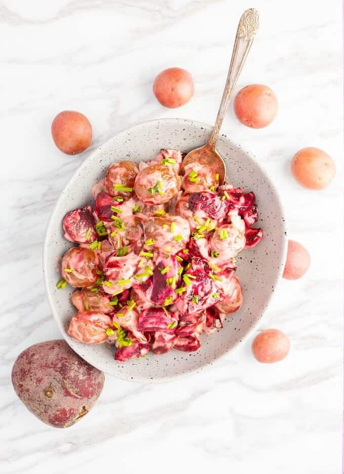 Roasted Beet Potato Salad in whitish bowl with spoon, Potatoes and beet around the plate on the white-gray table