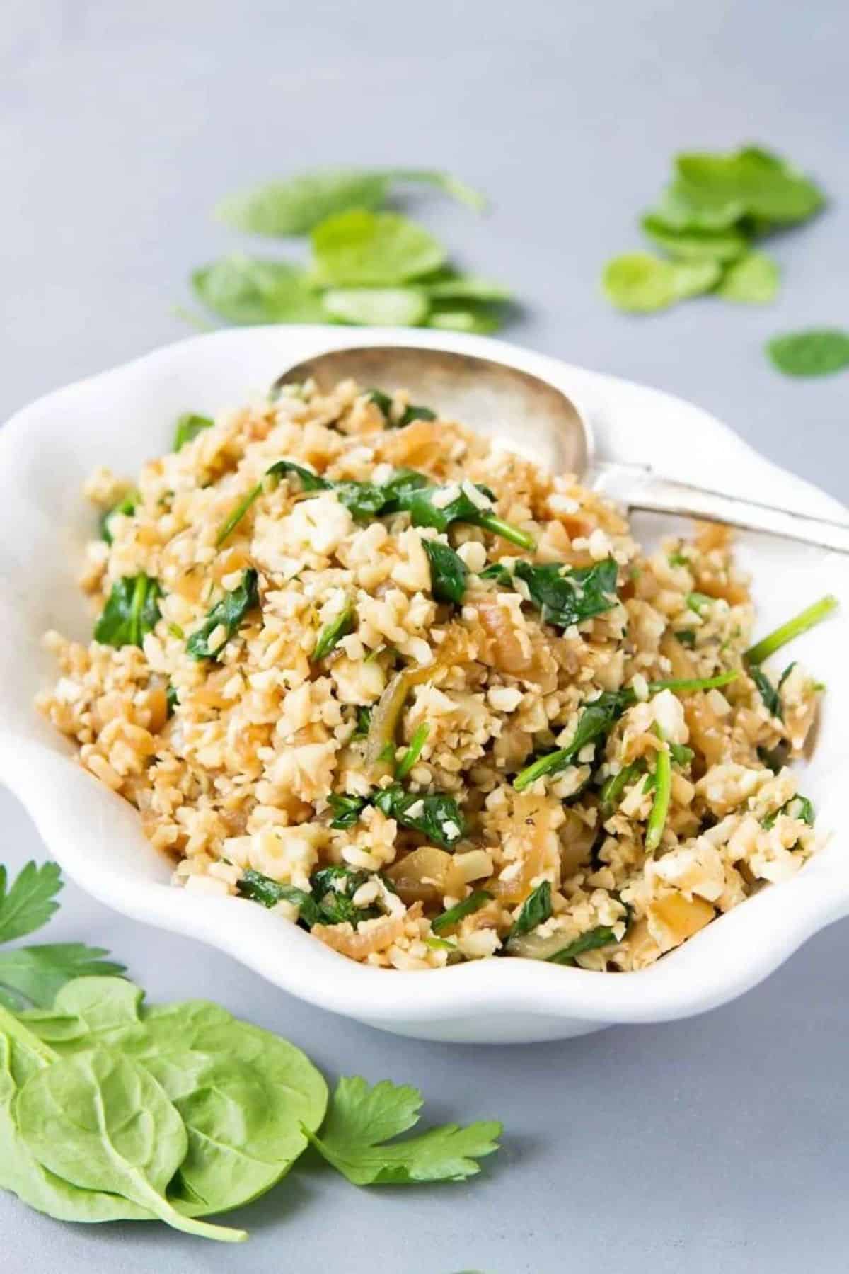 Healthy Sauteed Cauliflower Rice in a white bowl with a spoon.
