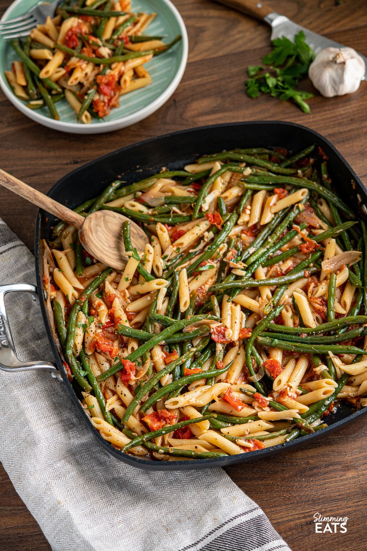 Delicious Roasted Green Bean and Tomato Penne Pasta in a skillet with a wooden spoon.