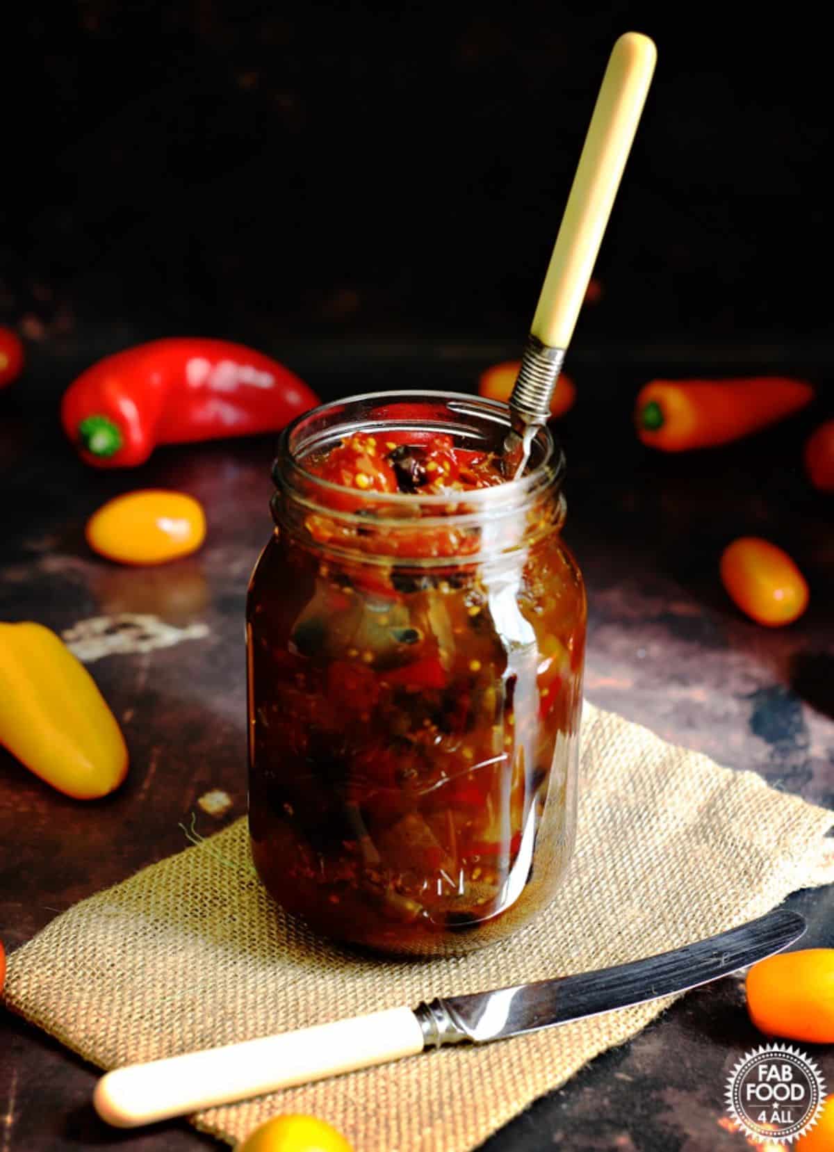 Juicy Spicy Baby Tomato and Sweet Pepper Chutney in a glass jar with a spoon.
