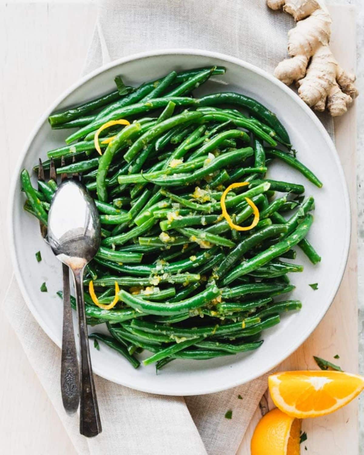 Fresh Orange Ginger Green Beans in a white bowl with a spoon and a fork.