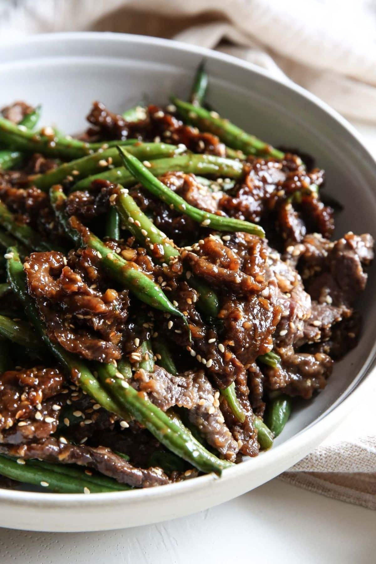 Juicy Sesame-Ginger Beef Stir Fry With Green Beans in a white bowl.