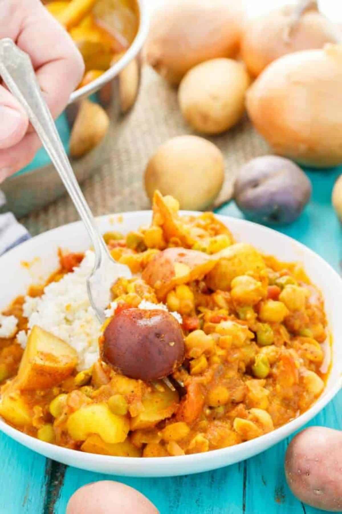 Scrumptious Vegan Potato Curry with Cauliflower Rice in a white bowl with a fork.