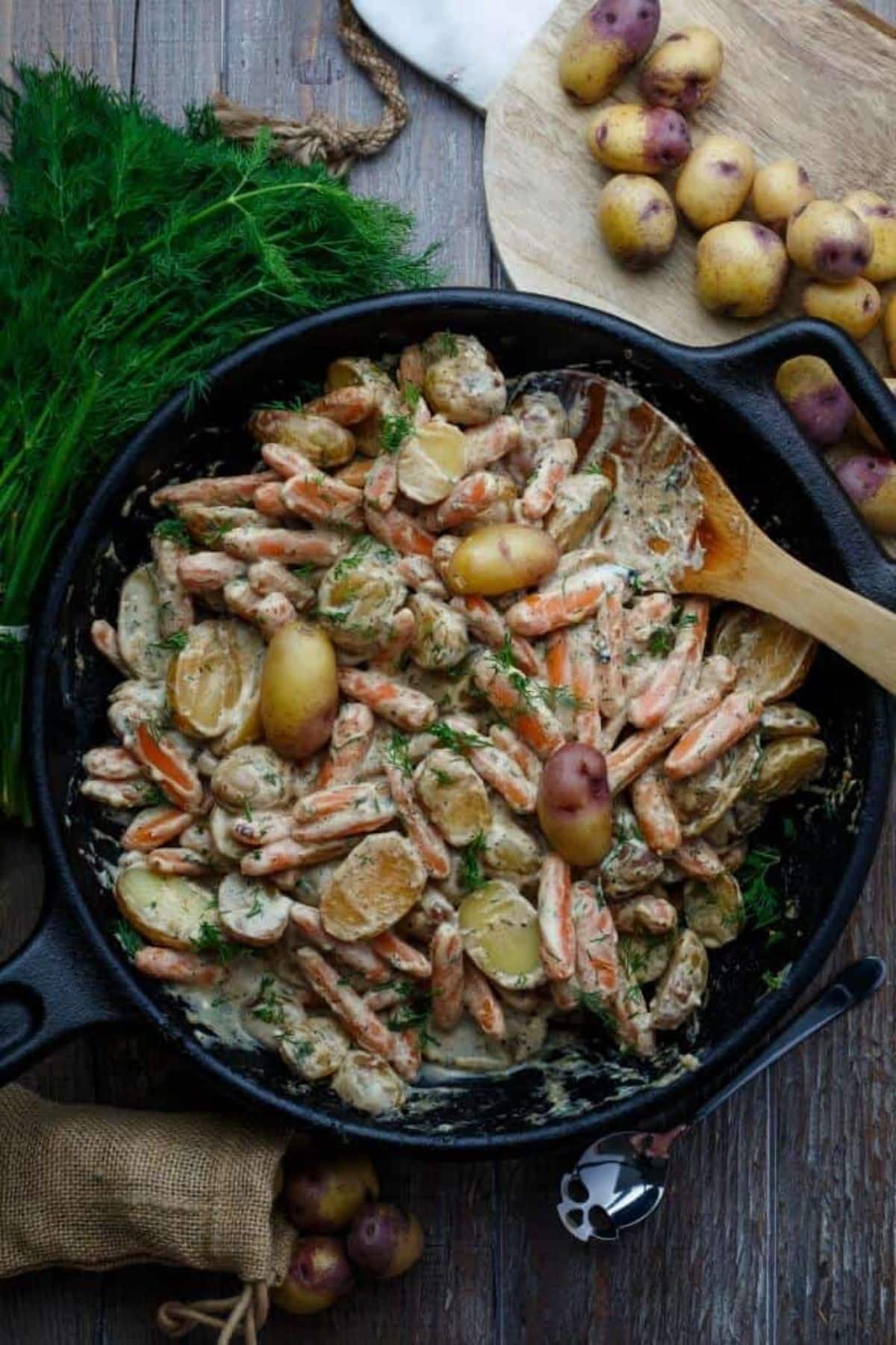 Creamy Sour Cream Lemon Potatoes and Carrots in a black skillet with a wooden spatula.