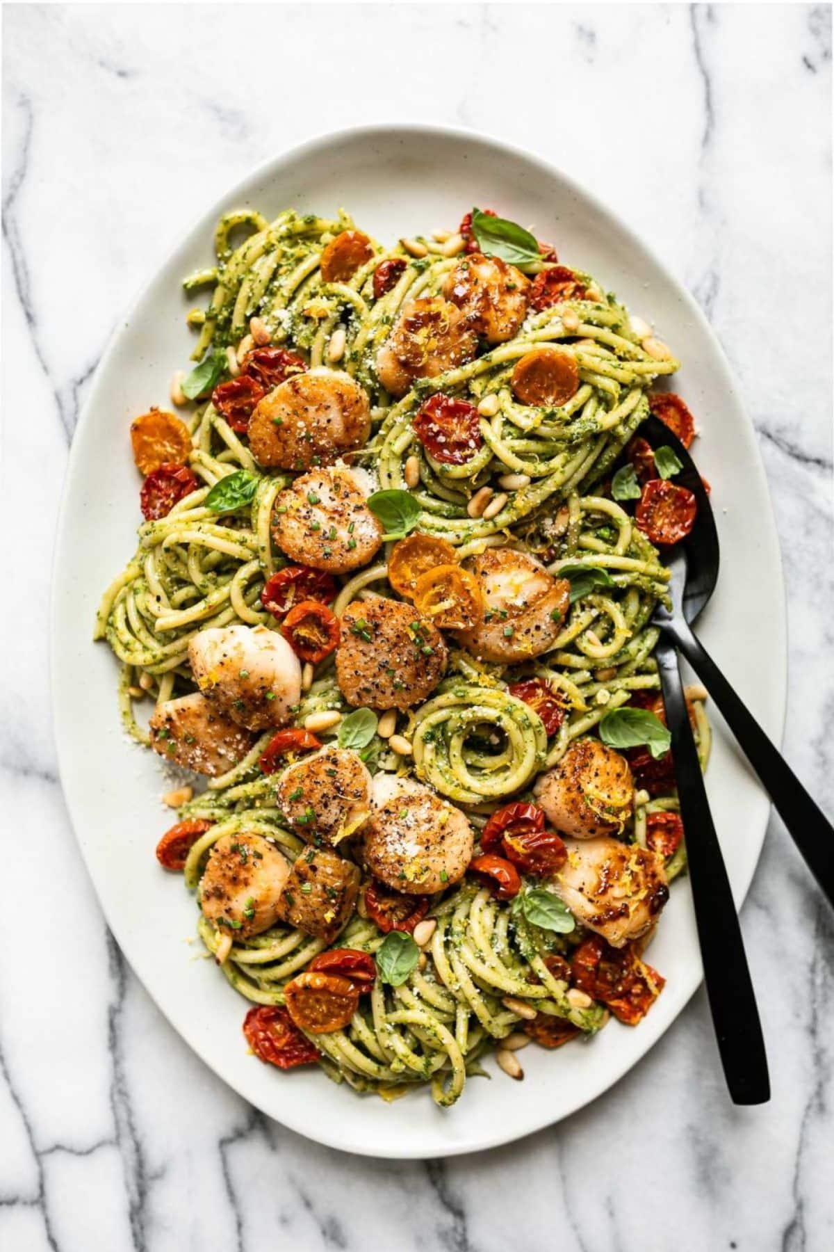 Scrumptious Pesto Scallop Pasta on a white tray with cutlery.