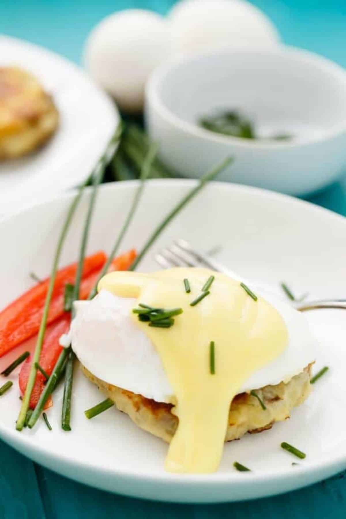 Flavorful  Eggs Benedict over Potato Pancake in a white bowl with a fork.