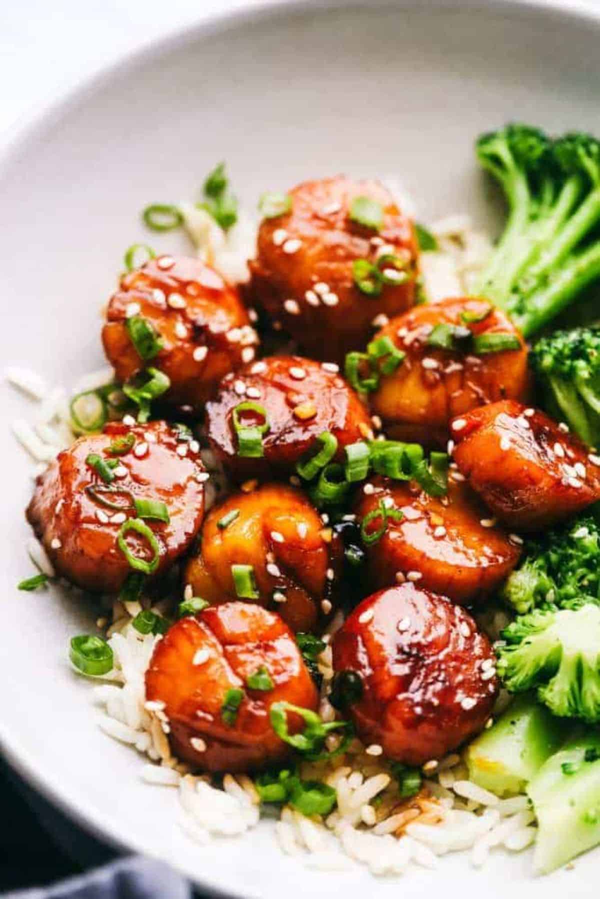 Juicy Honey Garlic Butter Scallops with veggies and rice in a white bowl.