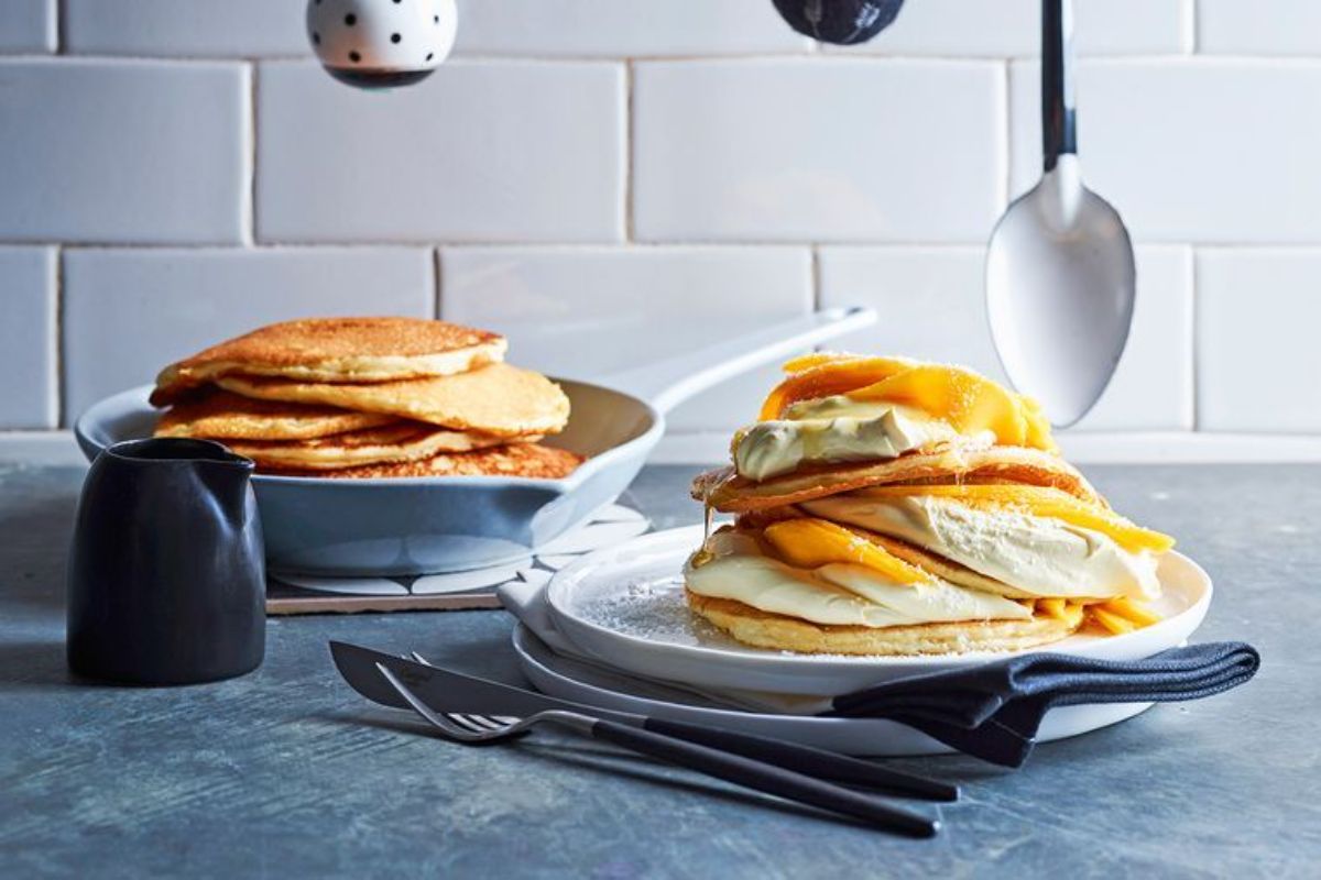 A pile of Mango and Coconut Pancakeson a white tray, another pile in a skillet.