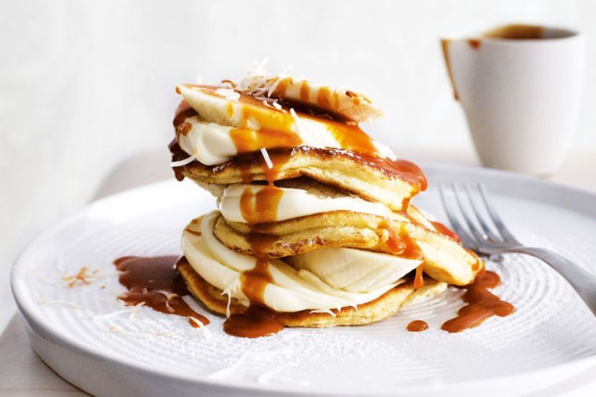 A pile of Coconut Pancakes with Banana and Creme Fraiche on a white plate with a fork.