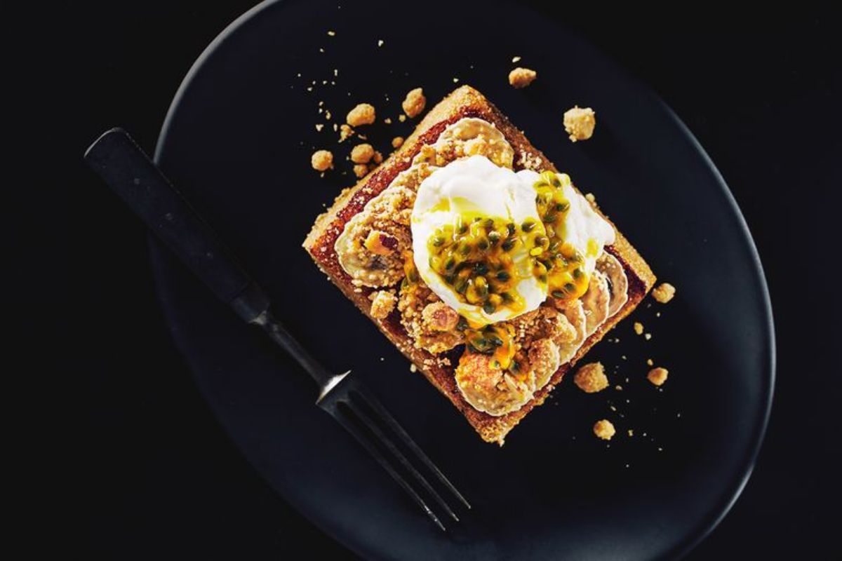 Mouth-watering Coffee-infused French toast with Banan, Nut Crumble, and Yoghurt o a black tray.