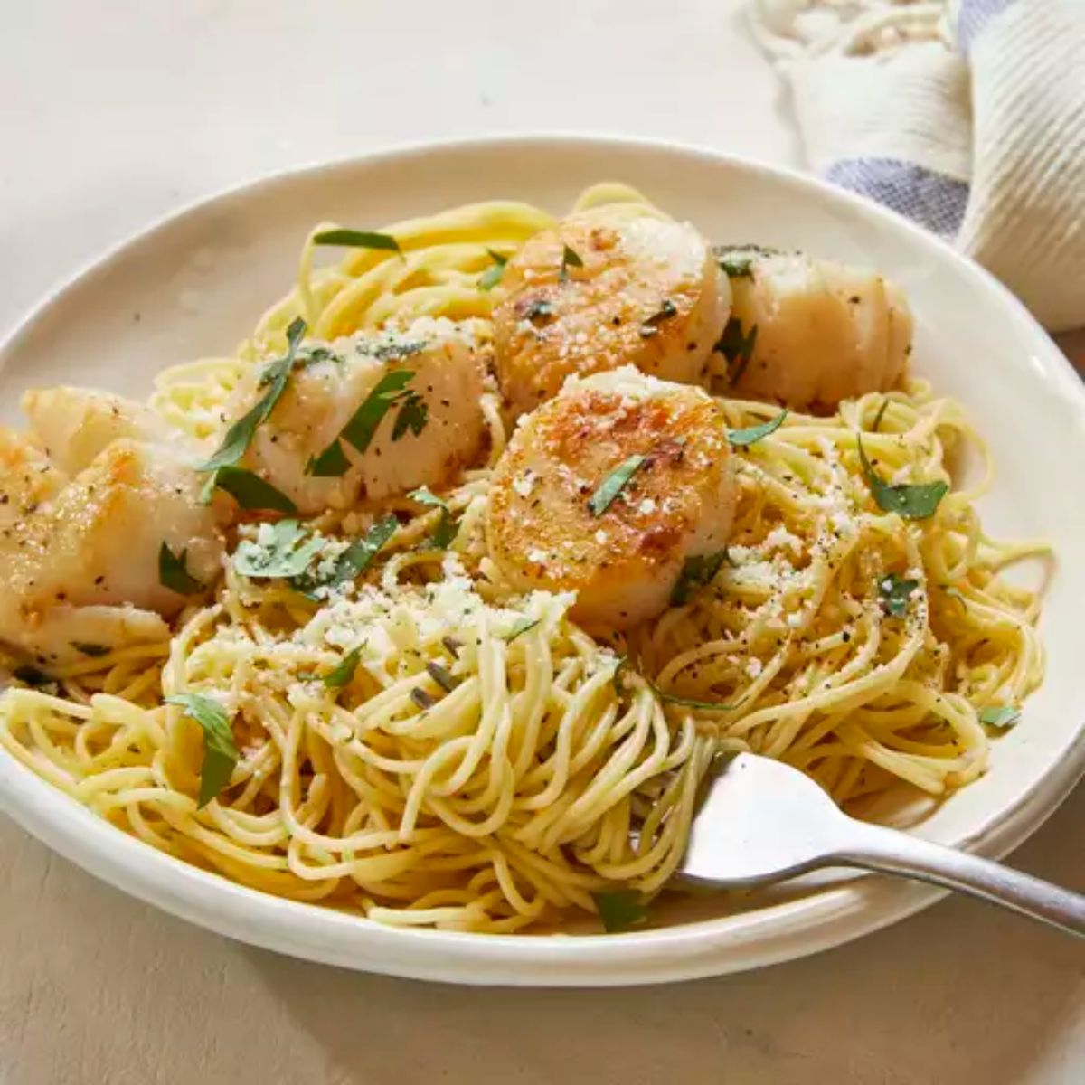 Tasty Savory Sea Scallops and Angel Hair Pasta in a white bowl with a fork.
